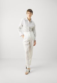 Witte linnen broek met een trekkoord in de taille, gecombineerd met een gestreept overhemd in wit en marineblauw. Zilveren sandalen met hakken maken de outfit compleet.