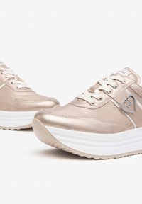 Baskets en rose gold métallique avec semelles blanches à plateforme, présentant un accent en forme de cœur, un design à lacets et une texture lisse.