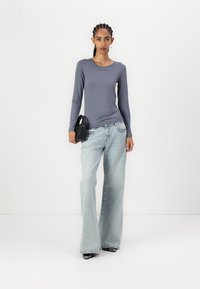 Long-sleeve gray top with a scoop neckline, paired with light-wash flared jeans and black pointed-toe heels, holding a small black bag.