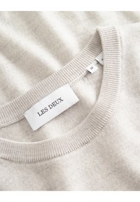 Beige, kerek nyakú pulóver, puha anyagból, bordázott nyakkal, a márka címkéjével, amelyen a "Les Deux" felirat és az "M" méret található.