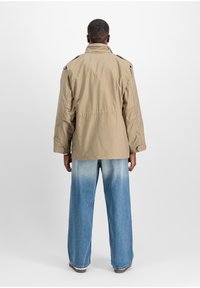 Beige outerwear jacket with epaulets, back pleat, and relaxed fit, paired with light blue wide-leg jeans featuring a gradual color fade.