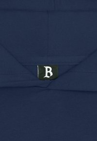 Marineblå hettegenser med en myk tekstur, med en brettet krage. Den indre merkelappen viser et hvitt "B" på svart bakgrunn.