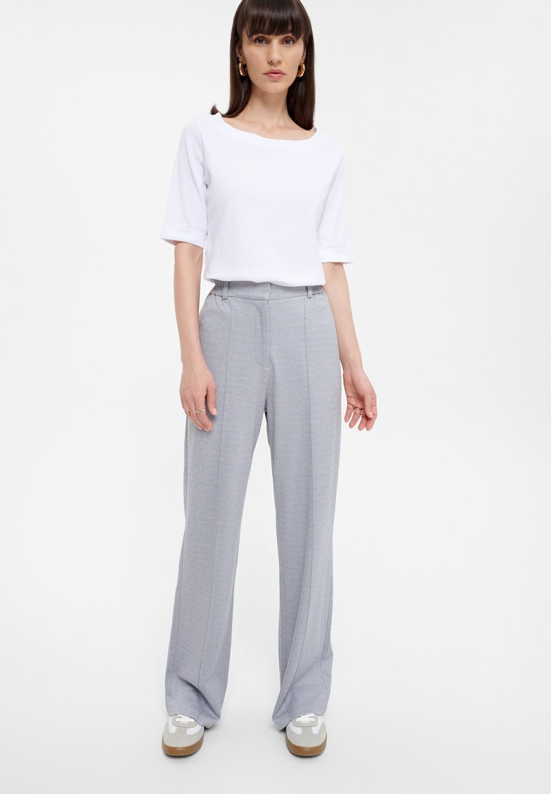 Witte top met korte mouwen, grijze wijde broek met verticale streepjes, en witte sneakers met grijze accenten. Glad stof textuur.