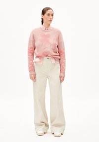 Helles rosa Sweatshirt mit Blumendesign, über einem hellen Hemd getragen, kombiniert mit lockeren beigen Hosen und weißen Turnschuhen. Glatte Texturen durchgehend.