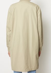 Lichtbeige lange jas met ribgebreide kraag en mouwen, met een gladde, matte afwerking. Eenvoudig ontwerp met zijzakken en een losse pasvorm.