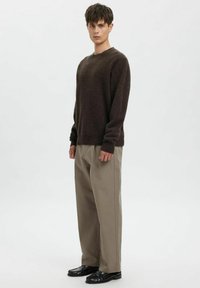 Rjavo pleten pulover z okrolim izrezom, kombiniran z bež širokimi hlačami in črnimi čevlji, ki ustvarjajo plasten, priložnostni videz.