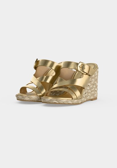 Sandales compensées dorées avec semelle plateforme tressée, brides croisées et fermetures à boucle réglables sur fond blanc.