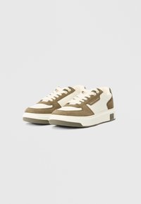 Tenisice s gornjim dijelom od zeleno-smeđeg nubuka, bijelim kožnim detaljima, perforiranim prstom i masivnom bijelom gumom. Imaju vezice i detalj s logotipom.