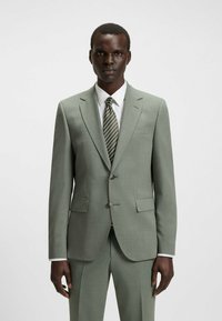 Helle grüne maßgeschneiderte Anzugjacke mit Revers, zwei Knöpfen und Taschen; kombiniert mit einem weißen Hemd und einer gestreiften Krawatte. Glatte Textur.