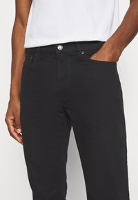 Vaqueros negros de corte slim, confeccionados en denim, con un diseño clásico de cinco bolsillos y cierre delantero visible con botón y cremallera.