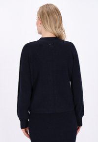 Dunkelblauer Pullover mit gerippter Textur, rundem Ausschnitt und Rückennahtdetails. Lange Ärmel und lockere Passform.