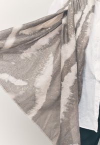 Sciarpa grigia e bianca in tessuto morbido e strutturato. Presenta motivi astratti e macchie dorate, rifinita con bordi sfrangiati.