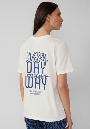 T-shirt en coton blanc avec un texte bleu au dos : "CHAQUE JOUR EST LA FAÇON PARFAITE VOTRE CORPS EST VOTRE MEILLEUR ACTIF." Manches courtes.
