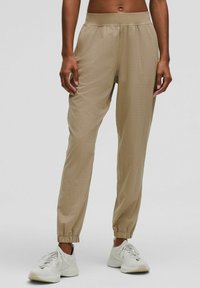 Beige jogger pants made of lightweight fabric, featuring a dotted pattern, elastic waistband, and cuffed ankles. Paired with white sneakers.