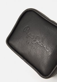 Bolsito de cuero negro con el logotipo en relieve de "Pepe Jeans London". Presenta una superficie texturizada y una forma rectangular redondeada.