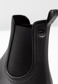 Svarta Chelsea-stövlar med en slät läderexterior och stretchiga tygpaneler på sidorna, med en metall-logotyp och kontrasterande sömmar.