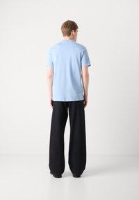 Light blue cotton t-shirt with short sleeves, paired with wide black trousers. Smooth texture and simple, unadorned design.