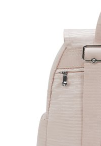 Soft pink fabric backpack features a textured surface, a side zippered pocket, and a prominent silver hardware accent on the strap.