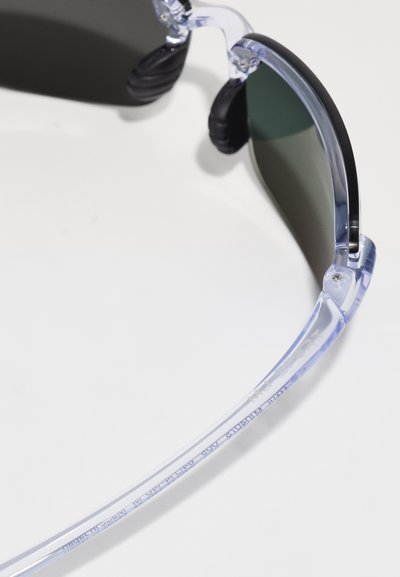 Klarer Plastik-Sonnenbrille mit dunkelgrünen Gläsern, kantigem Design, Gummi-Haltegriffen an den Bügeln und gravierter Markenkennung an der Bügelinnenseite.