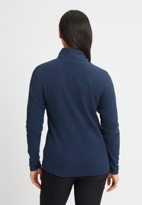 Dunkelblauer Fleece-Pullover mit hohem Kragen und langen Ärmeln. Weicher Stoff, figurbetonter Schnitt und dezentes Logo-Detail am Kragen.
