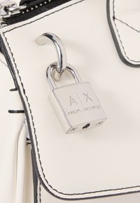 Sac à main en simili cuir blanc avec des coutures noires, orné d'un charm en forme de cadenas en argent gravé "A|X ARMANI EXCHANGE."