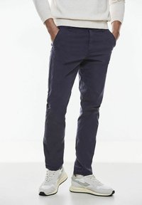 Pantalones slim-fit de color navy hechos de tela ligera, con bolsillos frontales y una textura suave, acompañados de zapatillas deportivas de color gris claro.