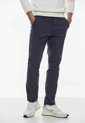 Pantalones slim-fit de color navy hechos de tela ligera, con bolsillos frontales y una textura suave, acompañados de zapatillas deportivas de color gris claro.