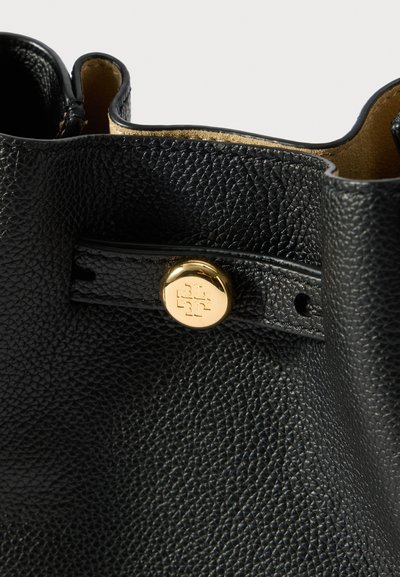 Czarna torebka z teksturowanej skóry z okrągłym, złotym zapięciem oraz wytłoczonym logo, pokazująca górną krawędź i podszewkę wnętrza.