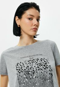 Grå t-shirt med et leopardprintgrafik i sort og sølv accenter. Rund halsudskæring og korte ærmer. Glat bomuldsstof.