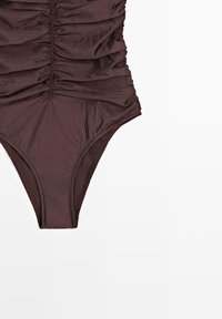 Bas et milieu de maillot de bain une pièce marron froncé sur fond blanc, montrant la texture du tissu et les détails des coutures.