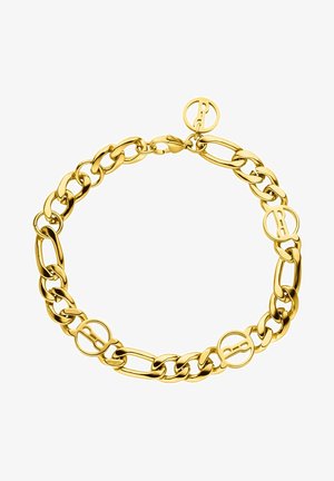Gros plan d'une personne portant un débardeur beige côtelé et un bracelet chaîne en or au poignet droit.