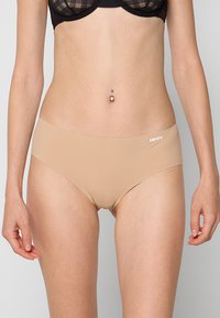 Bragas tipo hipster beige de DKNY con textura suave y cintura elástica. Presentan un pequeño logo blanco en el lado izquierdo delantero.