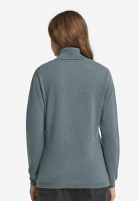 Hellblauer, langärmeliger Rollkragensweater aus weichem, strukturiertem Stoff mit gerippten Bündchen und Saum. Er hat eine lässige Passform und minimale Nähte.