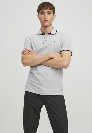 Polo de color gris claro con cuello negro y acentos en las mangas, con tres botones y un pequeño logo en el lado izquierdo del pecho.