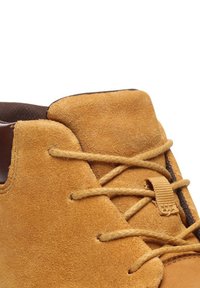 Beige Wildlederschuh mit niedrigem Profil, ausgestattet mit braunen Schnürsenkeln, einem einfachen Schnürsystem und einer weichen Textur.