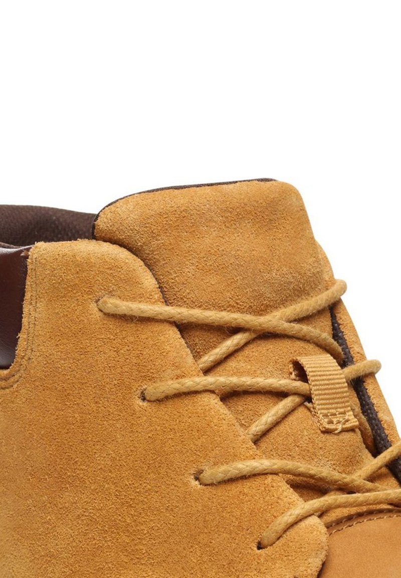 Scarpe in suede beige con design a profilo basso, caratterizzate da lacci marroni, un semplice sistema di allacciatura e una superficie morbida e testurizzata.