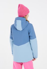 Giacca blu e azzurro con cappuccio, caratterizzata da un design a zigzag. Accompagnata da un berretto rosa lavorato a maglia. Texture liscia, progettata per il calore.
