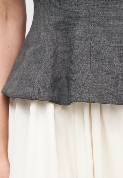 Γκρι τοπ πεπλούμ από υφή υφάσματος, με εφαρμοστό μπούστο και φαρδιά χαμηλή άκρη, σε συνδυασμό με λευκή πλισέ φούστα.