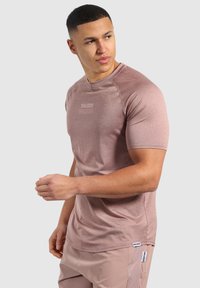 Camisa deportiva de manga corta en rosa claro con tejido texturizado y cuello redondo. Presenta el logo de la marca en un estampado sutil en la parte frontal.