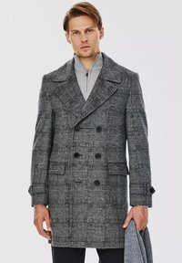 Szary w kratę dwurzędowy płaszcz z dużymi klapami, czarnymi guzikami i bocznymi kieszeniami. Noszony na szarym swetrze z wysokim kołnierzem.