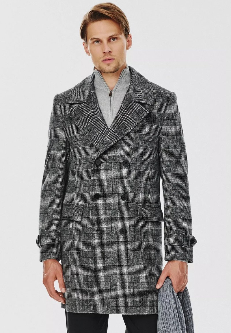 Szary w kratę dwurzędowy płaszcz z dużymi klapami, czarnymi guzikami i bocznymi kieszeniami. Noszony na szarym swetrze z wysokim kołnierzem.