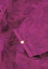 Paarse stof met ingewikkelde borduurwerk van bloemen en harten. Bevat een decoratieve gouden accent met een sterontwerp en uitgesneden details langs de rand.