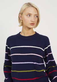Granatowy sweter z wielokolorowymi poziomymi paskami (różowy, biały, zielony, czerwony). Miękka tekstura, okrągły dekolt i rękawy raglanowe.