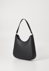 Černá kožená kabelka přes rameno s zakřiveným horním okrajem a jedním popruhem, stojící na jednoduchém světlém pozadí.