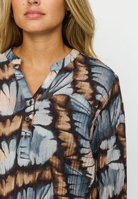 Mönstrad skjorta med knappar i blå, brun och crème tie-dye-design, med mandarin-krage och tre synliga knappar. Texturerat tyg.