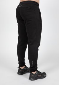 Zwarte sweatpants met een elastische tailleband, taps toelopende benen en zijzakken. Voorzien van witte branding op het onderbeen. Zachte stoftextuur.