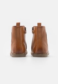 Bottines en cuir tan avec un bout rond, des fermetures éclairs sur les côtés et des languettes à l'arrière ; texture lisse et minimalisme des détails de couture.