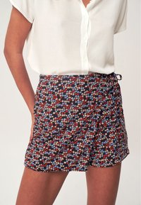 Shortsit, joissa on kukkakuosi tummalla taustalla, ja joissa on pienet siniset, punaiset ja valkoiset kukat. Valmistettu kevyestä kankaasta, jossa on sidottu vyötärö.