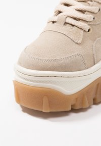 Beige Wildleder-Sneaker mit dicker weißer Zwischensohle und beige-gummierter Außensohle. Verfügt über strukturierte Akzente und Schnürverschluss mit passenden Schnürsenkeln.
