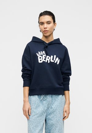 Marineblå hættetrøje med frontprint, der lyder "LALA BERLIN" i hvide, bløde bogstaver. Har snøre i hætten og ribbede ærmekanter.